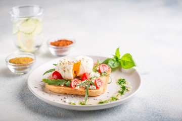 French breakfast concept. Poached egg on toasted bread with cherry tomatoes, cheese and herbs on a boiled background