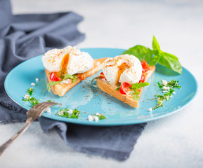 Two poached eggs on toasted toast with cherry tomatoes, cheese and herbs on a large blue plate