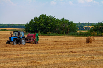 A tractor with a trailed bale making machine collects straw rolls in the field and makes round large bales