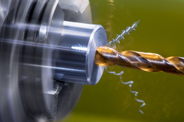 Rotating lathe detail. Screw drill bit cutting axial hole in metal workpiece. Artistic close-up of...