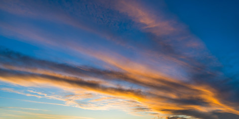 Panoramic orange illuminated sky background in evening dusk view. Dramatic sunset on blue striped cloudscape with sunlit fiery clouds. Scenic natural panorama of afterglow light. Ecology and weather.