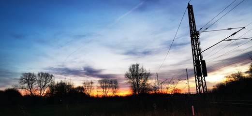 A fantastic sunset with red yellow orange and purple tones with dramatic cloud formation over green meadows with bare trees in January on the island of R&uuml;gen