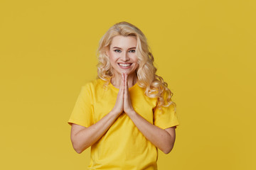 Photo of a happy young blond woman standing isolated over yellow wall background. Looking at the camera showing the direction of copy space.