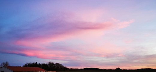 A fantastic sunset with red yellow orange and purple tones with dramatic cloud formation over green meadows with bare trees in January on the island of R&uuml;gen