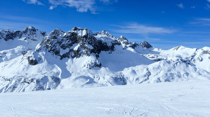 Fototapeta na wymiar Alpine snowy peaks panorama with slopes, off piste on fresh powder in Zurs winter sport resort, Alps, Arlberg, Austria, on a sunny cold day .