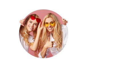 Portrait of two young happy, shocked women in the heart shape sunglasses looking throth the white hole in the wall. Big sale. Funny faces. Empty space for text