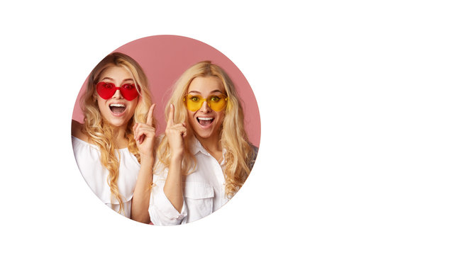 Portrait of two young happy, shocked women in the heart shape sunglasses looking throth the white hole in the wall. Big sale. Funny faces. Empty space for text