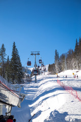 Sunny morning on the mountain, there are not many skiers on the ski slope. The cable car is just above the ski slope and the pine forest is all around.