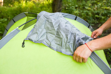 Man installing tent. Material protecting from rain. Tourist outdoors. Camping in the forest.