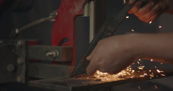Blacksmith grinding piece of iron on belt sander making knife sparks flying dark eerie closeup