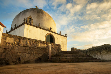 Socorro Chapel in Vila do Conde, Portugal, lit by the sunset and a sky with clouds in the background.