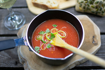 Hearty tomato soup in a saucepan with spring onions and herbs. Rustic arranged