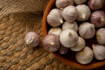 A lot of solo garlic in clay plate on straw mat and textile flat lay