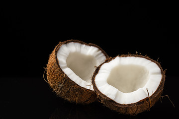 Coconut on a black background. Two halves of a nut. Coconut chopped in half. White flesh.