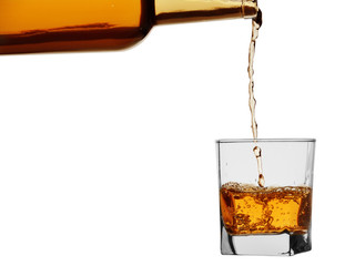 Whiskey or brandy from a bottle is poured into a glass. Isolated on a white background