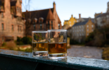 Scotch single malts or blended whisky spirits in glasses with old houses of Edinburgh on...