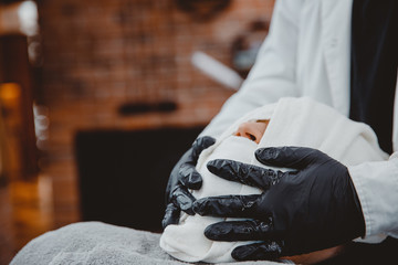 Obraz premium Barber steam face skin of man with hot towel before royal shave in Barbershop