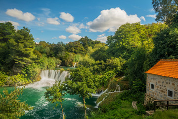 Fototapeta na wymiar Waterfall and old stone house in Krka National Park, Croatia. House next to Krka waterfall.