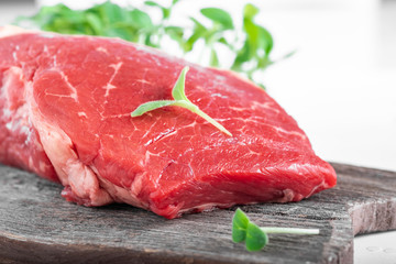 Fresh juicy piece of fresh beef with greens on a wooden Board on a white wooden background.