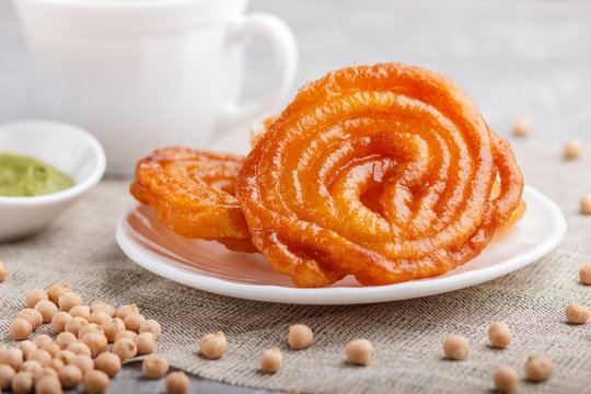 traditional indian candy jalebi in white plate with mint chutney on a gray concrete background. side view.