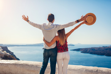 Valentines day. Couple in love enjoying view during honeymoon in Santorini island, Greece. People raising arms in Thera.