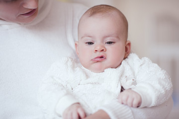 Little baby under 1 year old with funny unsatisfied expression on face sitting on mother hands in bed closeup.