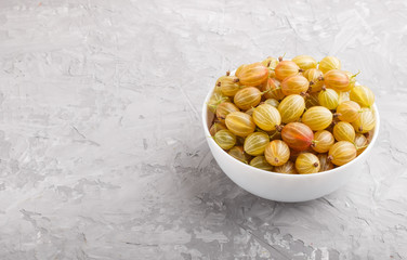 Fresh green gooseberry in white bowl on gray concrete background. side view.