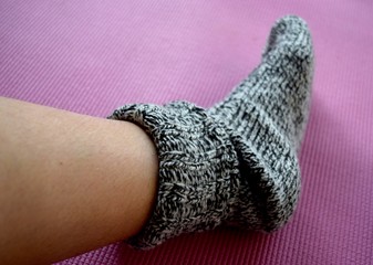 Woolen sock on female leg with long dark hair on pink background.