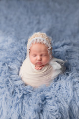 the first photo session of a newborn. newborn baby girl cocoon pose on blue background