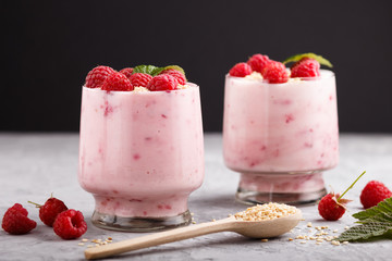 Yoghurt with raspberry and sesame in a glass and wooden spoon on gray and black background. side view.