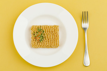 A plate of noodles on a yellow background. Top view.