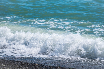 Sea wave with foam on a pebble beach.