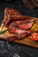 Close up sliced medium rare grilled beef steak with corn and tomato, pepper and rosemary on meat...