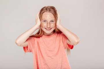 Inclusive Beauty. Girl with freckles standing isolated on grey covering ears smiling cheerful