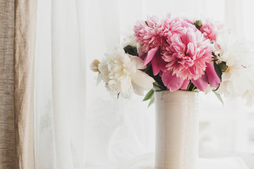Happy Mothers day. Lovely peony bouquet in sunny light on rustic wooden window sill. Stylish pink and white peonies in vase on wooden background. Copy space. Hello spring.