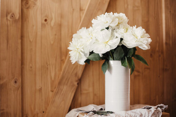 Happy Mothers day. Stylish peony bouquet in white ceramic vase on linen fabric with scissors on rustic wooden background.White peonies rural still life. Hello spring wallpaper. Space