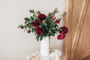 Stylish peony bouquet in white ceramic vase on linen fabric on rustic wooden background. Red and pink peonies rural still life. Hello spring wallpaper. Happy Mothers day. Space text