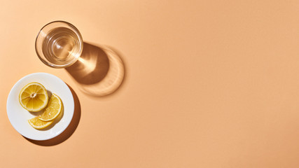 Glass with crystal clear water and a saucer with lemon slices isolated on orange. Orange background. Top view.