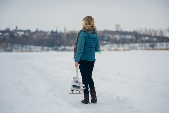 Young girl blonde showing giving ice skates for winter time ice skating sport activity happy smiling on a sunny snowy background. copy space