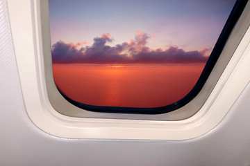 beautiful sky landscape of red sunset with clouds and sea below through the porthole of a plane, travel concept