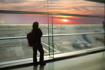female passenger, waiting for his flight, stands at the window and looks at the airport runway, a travel concert