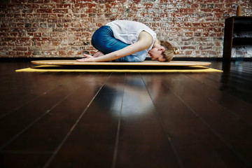 Middle aged woman resting on child pose yogaboard in yoga class. Healthy lifestyle concept