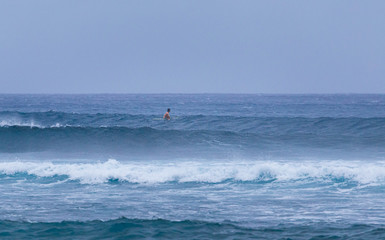 Lone surfer looking out to sea as he waits for waves in rough conditions
