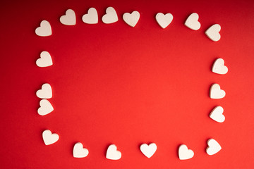 Top view of white wooden hearts on the red paper background. Flat lay for Valentine's Day. Concept of love...