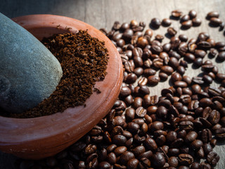 Black coffee ground in a clay mortar and in grains on the surface of a wooden table in sunny rays.