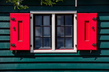 Fototapeta na wymiar bright red wooden window shutters at a green wooden wall and misty windows on a sunny day