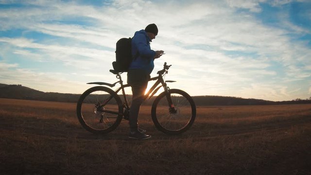 The silhouette of the mountain bicycle rider on the hill with bike at sunset. Sport, travel and active life concept.