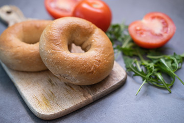 Bagels on a wooden table with tomatoes and rocket  on background. Close up view.