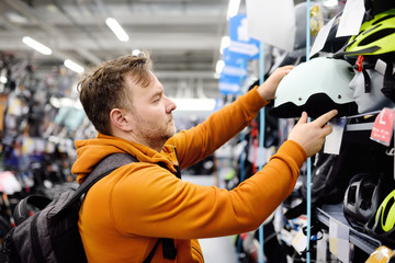 Middle age man choosing bicycle helmet in sport store.