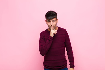 young handsome man looking serious and cross with finger pressed to lips demanding silence or...
